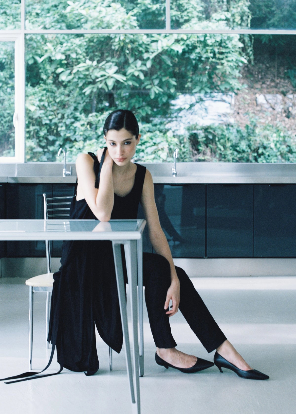 Model in a black dress seated beside a table wearing black pumps.