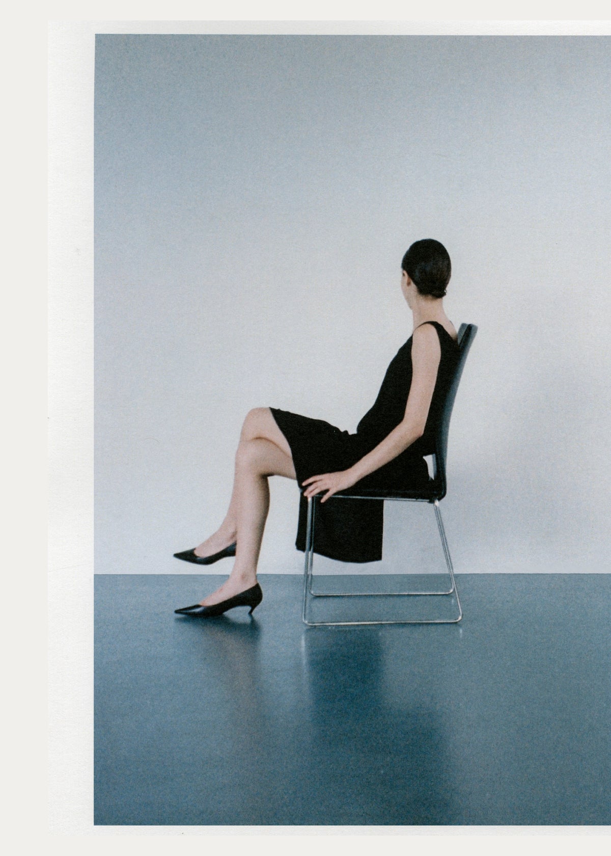 Rear view of a model seated in a black dress and black pumps.