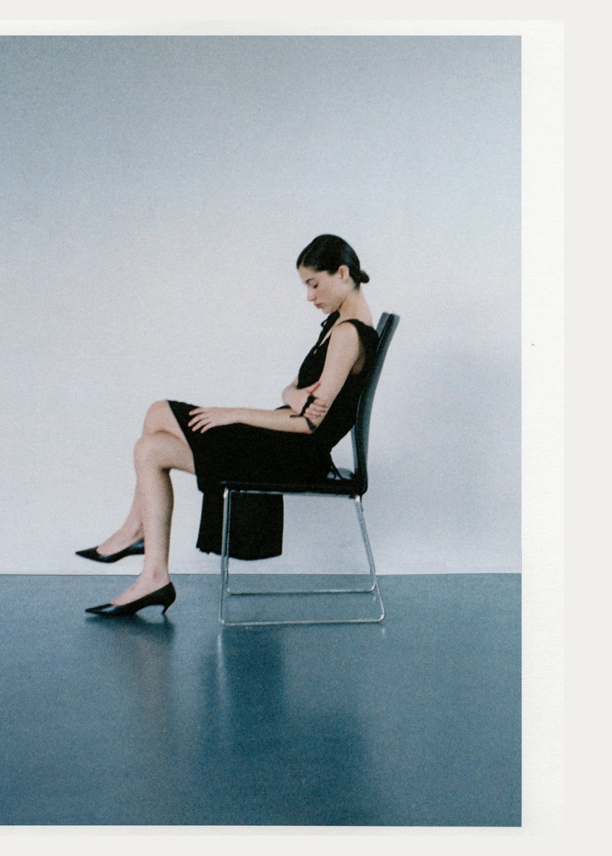 Side view of a seated model wearing a black dress and black pumps.