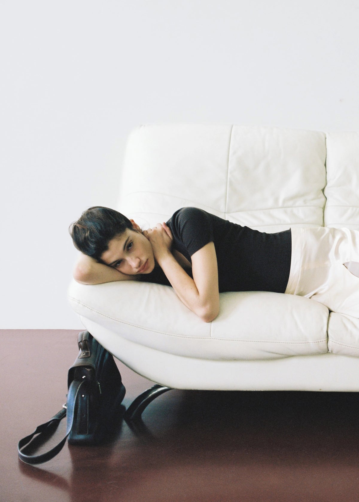 Model reclining on a white sofa with black pumps beside it.