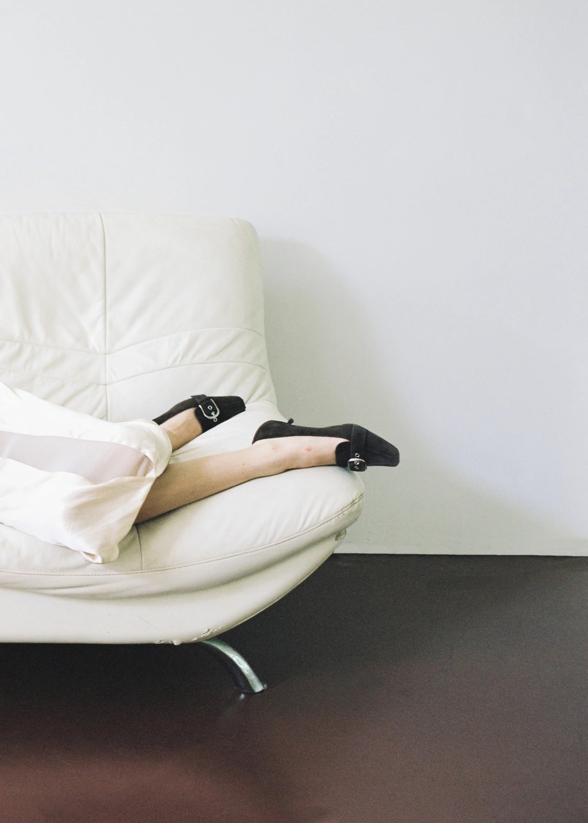 Detail of a white skirt and black pumps on a white sofa.