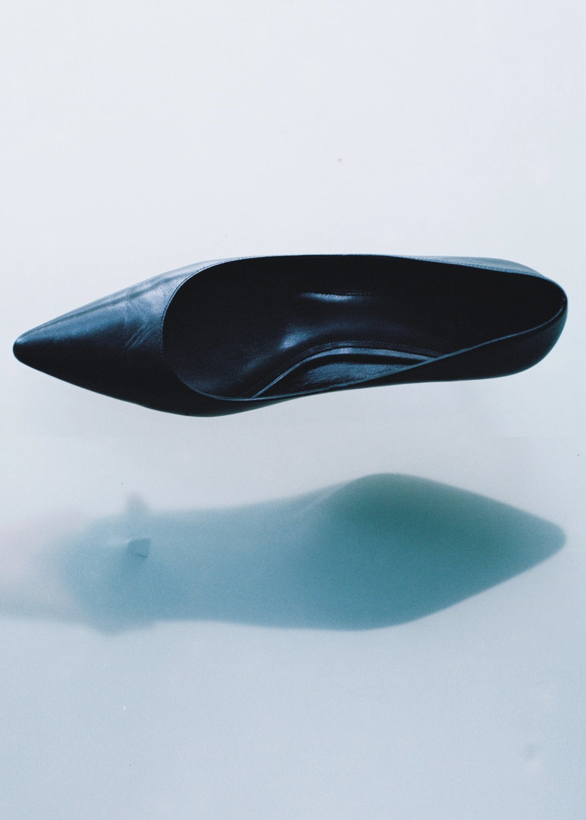 Black pointed-toe shoe casting a shadow on a pale surface.