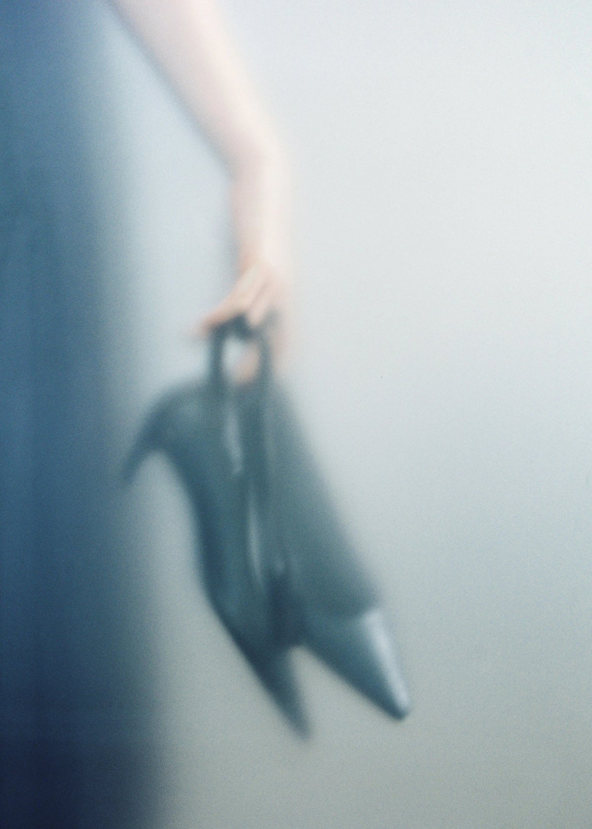 Soft-focus detail of a hand holding black pointed-toe shoes.
