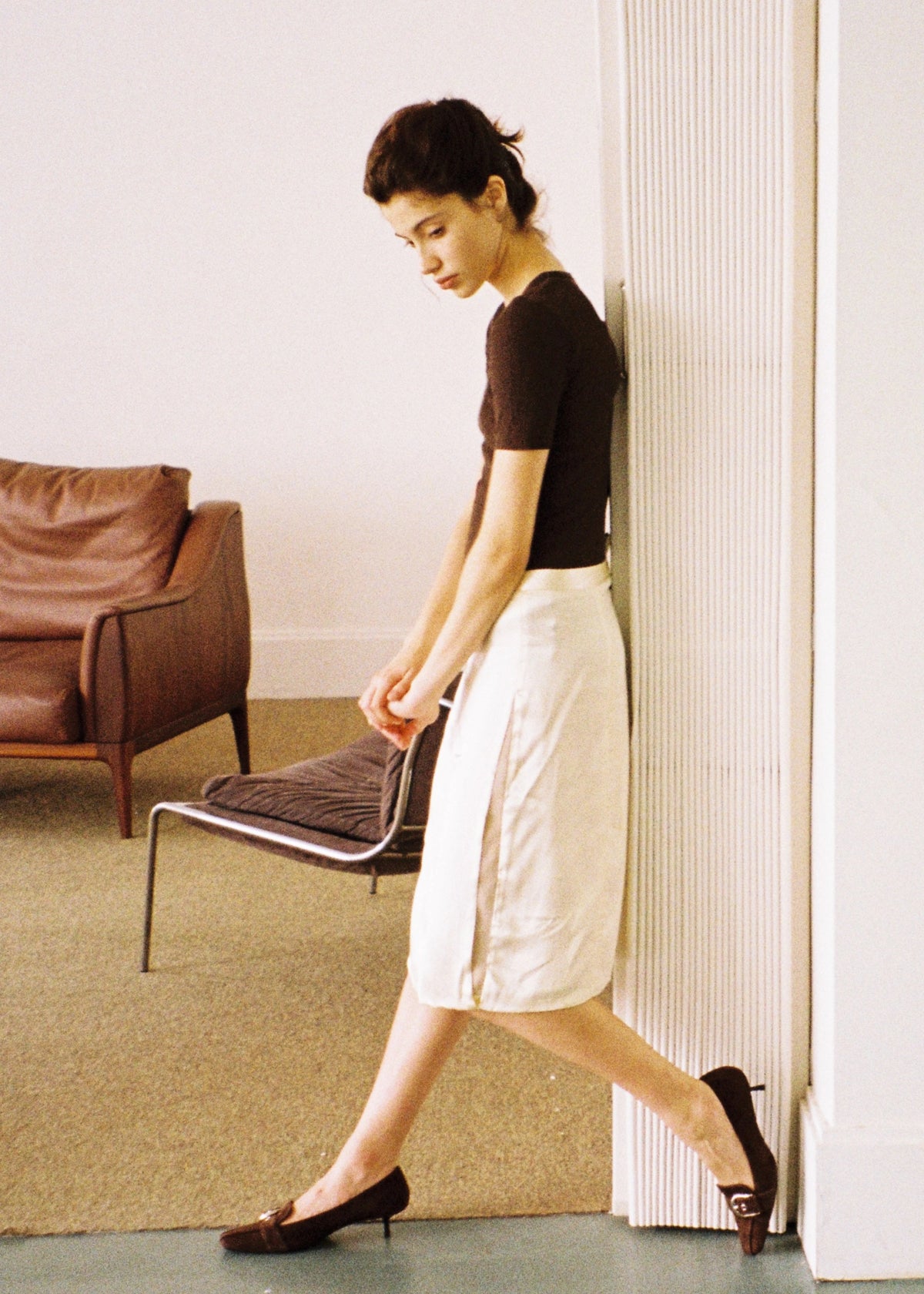 Model in a dark top and white skirt walking across a red floor.