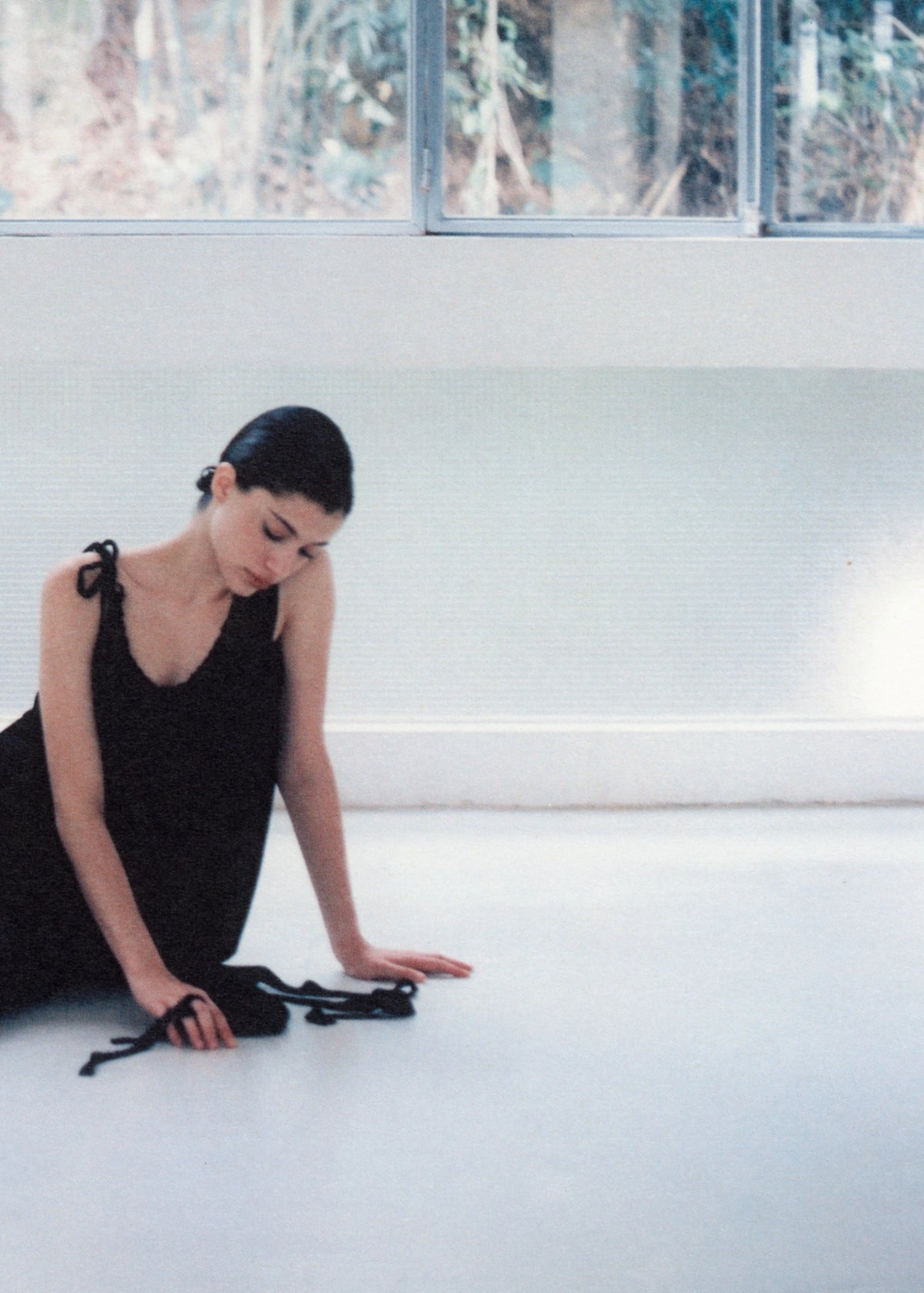 Model in a black dress seated on the floor beside black pumps.